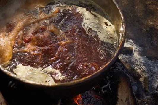 Thick, rich organic molasses bubbling in a cast-iron pot over a roaring log fire, symbolizing natural energy, slow-burning carbohydrates, and ancestral nutrition for sustained insulin balance and metabolic health. 