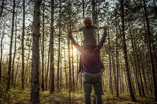 A father and son in the wilderness, teaching survival skills—symbolizing the greatest gift of health, wisdom, and resilience for future generations.